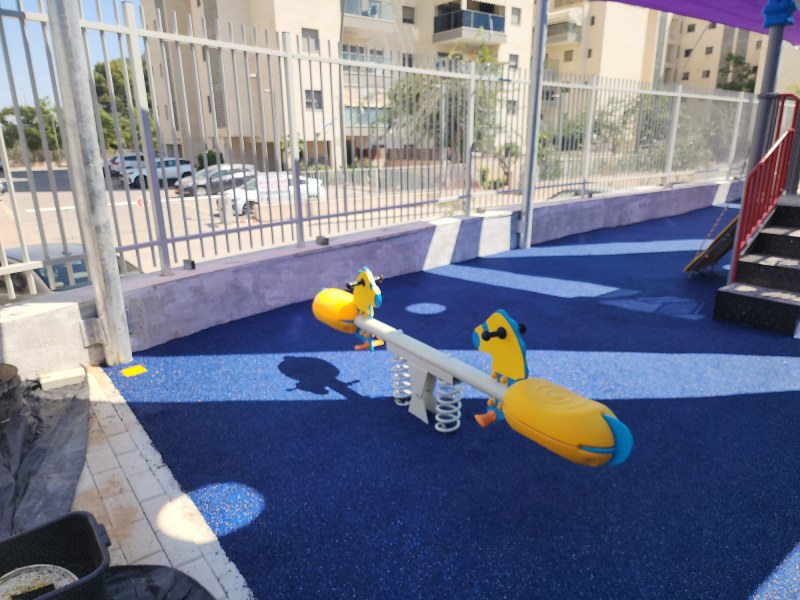 משטח גומי כחול בחצר גן ילדים עם מתקן משחק